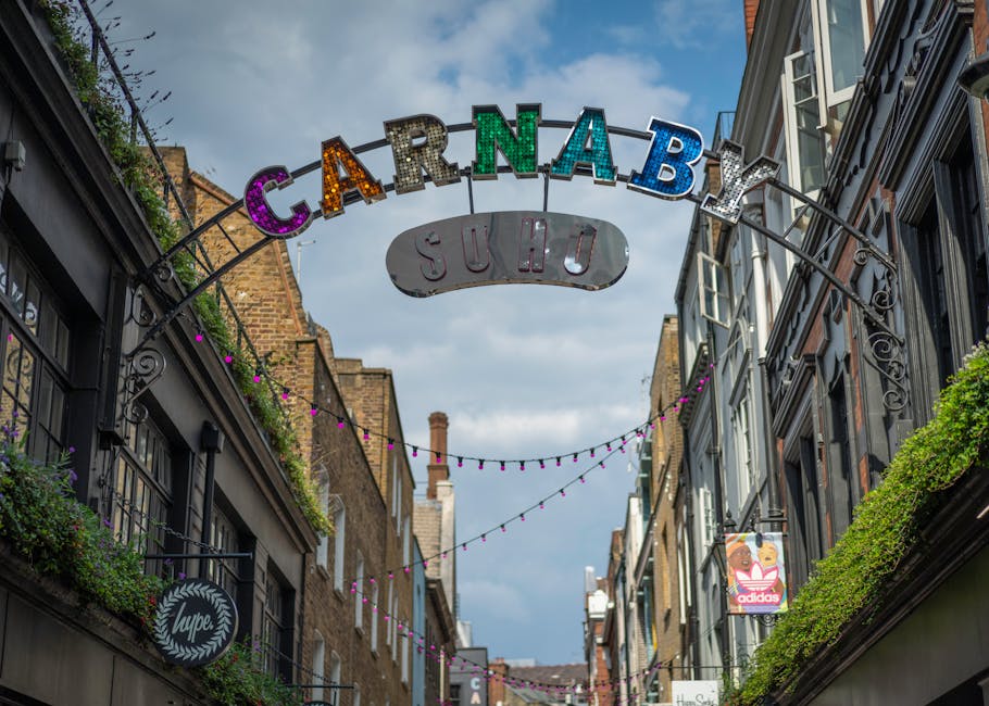 Nighttime view of Carnaby Street in Soho, W1, featuring illuminated colorful marquee letters spelling 'CARNABY' mounted on an archway above the street. The street scene includes traditional brick and