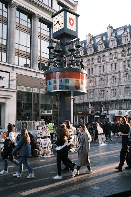 A tall wooden pole displaying multiple coats of arms and crests, including a prominent red shield with a white cross at the center, situated at a busy intersection with a red traffic light on the righ